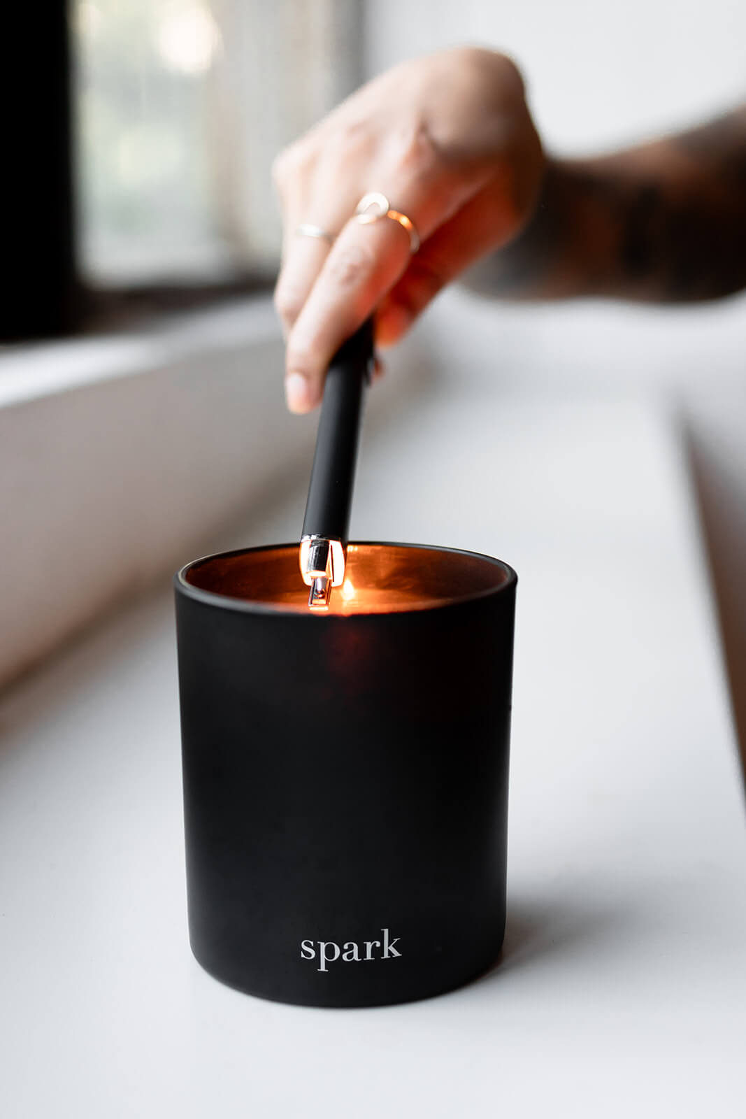 Person lighting a Spark Candles 10oz classic black glass candle 
