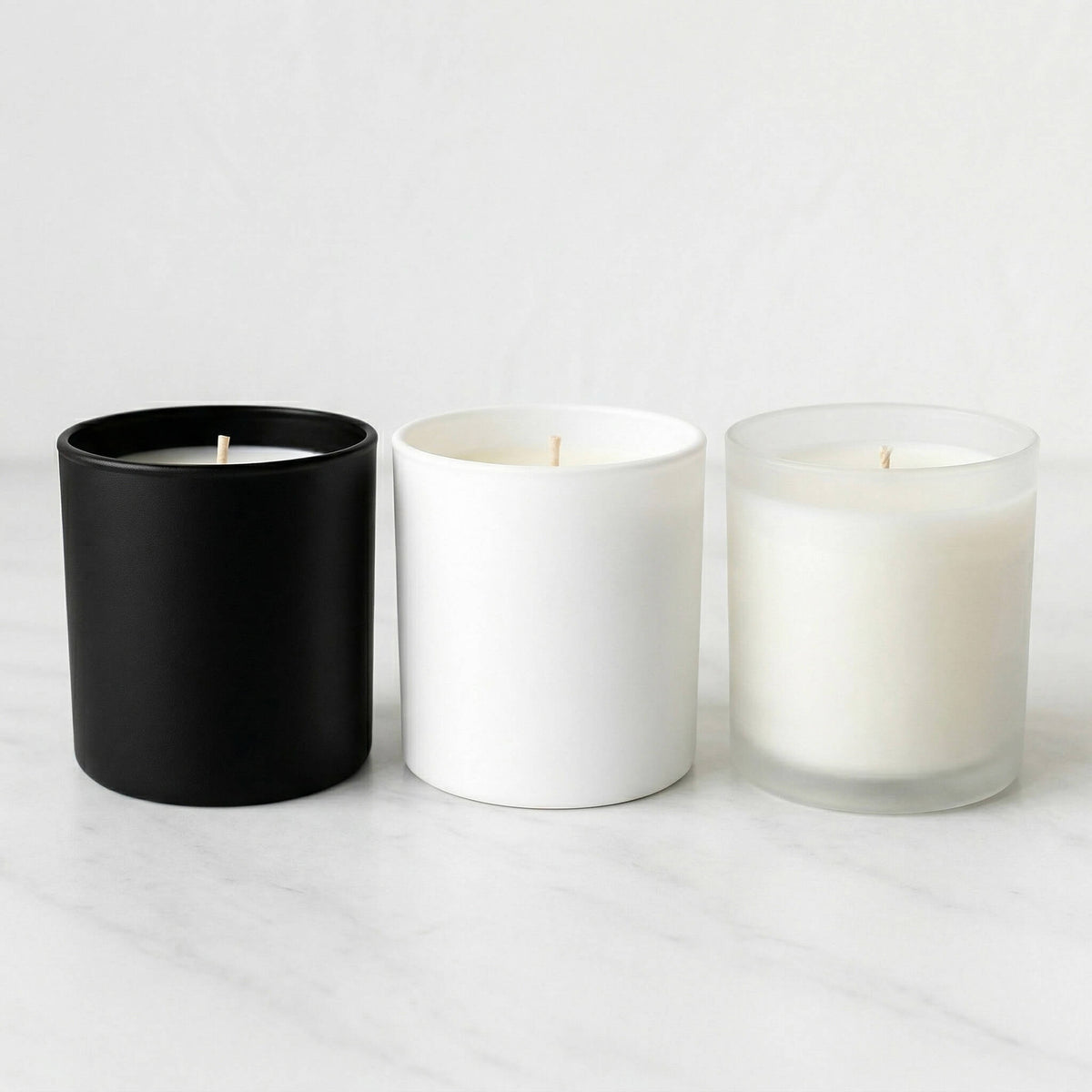 Three candles in black, white, and clear containers on a light gray background
